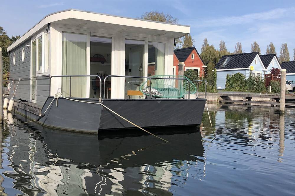 Modern houseboat in quiet harbor close to the Ijsselmeer with Sups and canoe in Stavoren, IJsselmeer