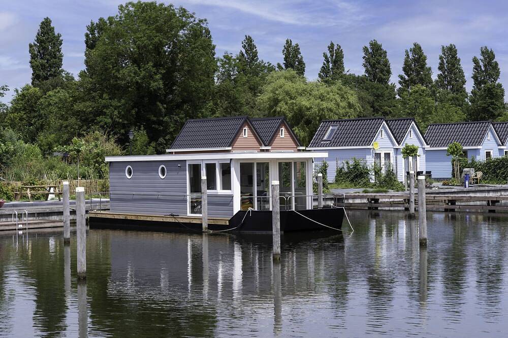 Modern houseboat in quiet harbor close to the Ijsselmeer with Sups and canoe in Stavoren, Ijsselmeer